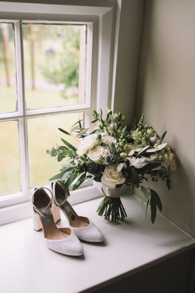 Ivory and green bridal bouquet in the window alongside wedding shoes