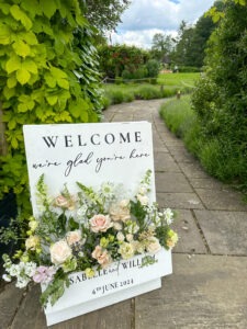 A board welcome sign for a wedding filled with netural florals