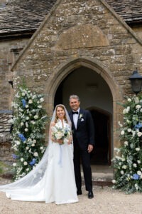 Broken arch outside of church filled with ivory and soft blue blooms